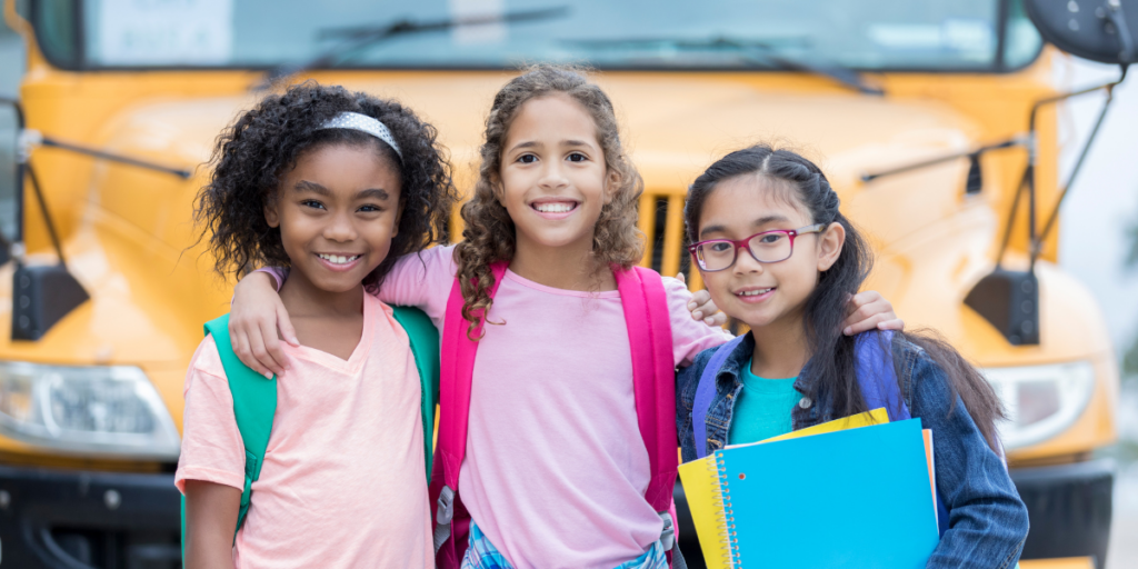 three students standing by school bus